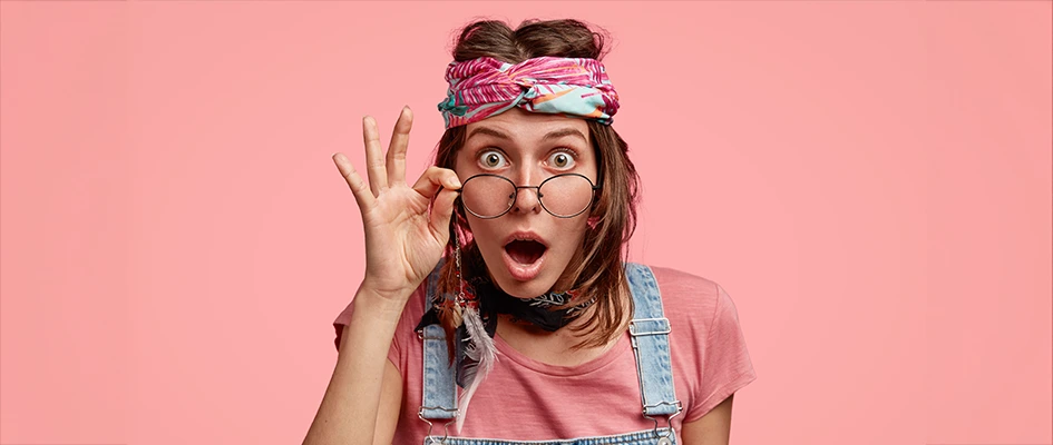 Femme au regard surpris avec des lunettes sur fond studio rose - Tester la sécurité d’un site web - Blog AE2